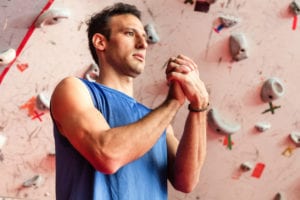 Caucasian man stretching sprained wrists on climbing site.