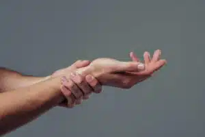 Man hand isolated on grey background. Close-up of man holding his wrist. Experiencing wrist pain.