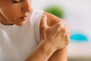 A woman is experiencing shoulder pain due to a frozen shoulder condition.